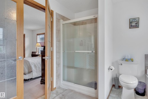 Glass-enclosed shower with a tiled surround, a white toilet, and light wood-finish French doors featuring textured glass panels - 16512 87 Street, Edmonton, AB 