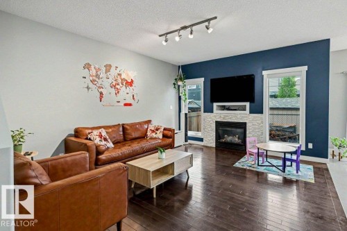 Living area featuring a gas fireplace with a stacked stone surround, dark wood-finish flooring, and a contemporary track lighting fixture - 13004 164 Avenue, Edmonton, AB 