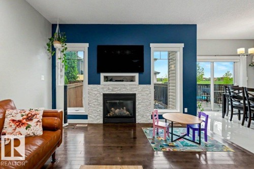 Living area featuring a modern linear fireplace with a mosaic tile surround, rich wood-finish flooring, and white trim windows - 13004 164 Avenue, Edmonton, AB 