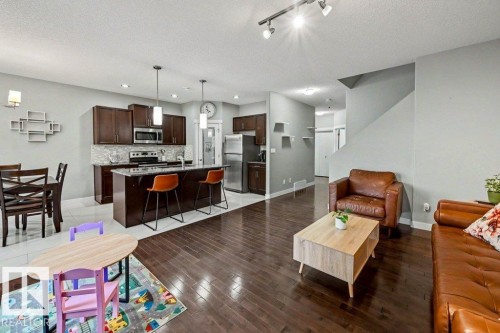 Open-concept living area with dark wood-finish flooring, a kitchen island with pendant lighting, stainless steel appliances, and a tiled backsplash - 13004 164 Avenue, Edmonton, AB 