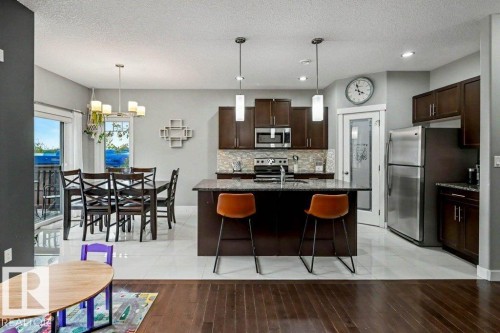 Open-concept kitchen and dining area featuring dark wood-finish cabinetry, stainless steel appliances, a center island with pendant lighting, and light-toned tile flooring - 13004 164 Avenue, Edmonton, AB 