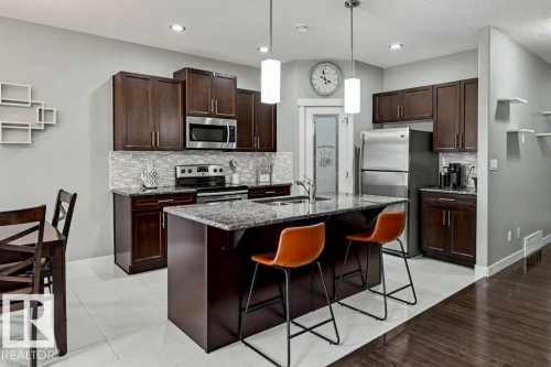 Kitchen featuring dark wood-finish cabinetry, stainless steel appliances, a tile backsplash, and a central island with a stone-finish countertop - 13004 164 Avenue, Edmonton, AB 