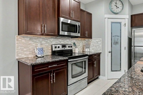 Kitchen featuring dark wood cabinetry, stainless steel appliances, granite countertops, and a mosaic tile backsplash - 13004 164 Avenue, Edmonton, AB 
