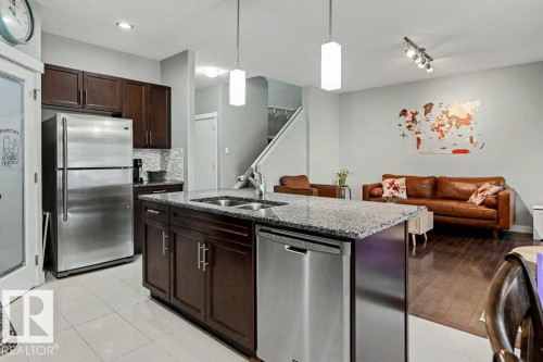 Open-concept kitchen featuring an island with a double sink, stainless steel appliances, dark wood cabinetry, and light-toned tile flooring - 13004 164 Avenue, Edmonton, AB 