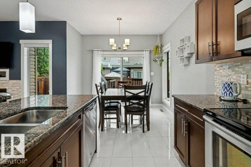 Kitchen featuring granite countertops, wood-finish cabinetry, stainless steel appliances, and white tile flooring - 13004 164 Avenue, Edmonton, AB 