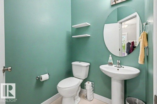 Bathroom featuring a pedestal sink with a chrome faucet, a wall-mounted circular mirror, and two floating wall shelves - 13004 164 Avenue, Edmonton, AB 