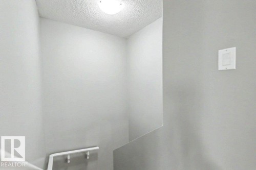 Stairwell featuring light gray walls, white ceiling, flush-mount lighting fixture, and a white handrail - 13004 164 Avenue, Edmonton, AB 