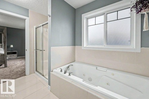 Bathroom featuring a built-in jetted tub, a separate shower with a sliding glass door, and a frosted window for privacy - 13004 164 Avenue, Edmonton, AB 