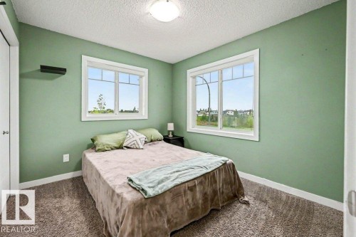 Bedroom featuring two large windows, carpet flooring, light green painted walls, white trim, and a flush mount ceiling light - 13004 164 Avenue, Edmonton, AB 