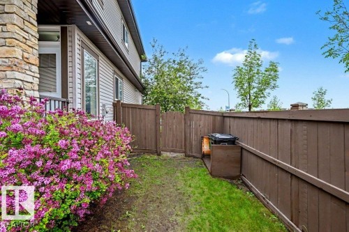 Private exterior space featuring a lush flowering shrub, a partial stone veneer facade, a side door with railing, vinyl siding, and a wood privacy fence - 13004 164 Avenue, Edmonton, AB 