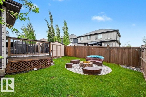 Expansive backyard featuring a wood deck with lattice skirting, a storage shed, and a stone patio with a built-in fire pit - 13004 164 Avenue, Edmonton, AB 