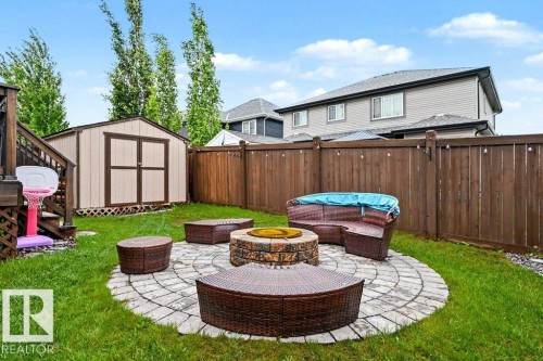 Expansive backyard featuring a circular paver patio with a stone fire pit, a wooden privacy fence, and a detached storage shed - 13004 164 Avenue, Edmonton, AB 