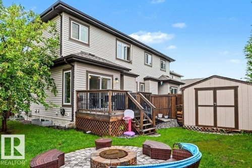 Expansive backyard featuring a stone-paver fire pit area, a multi-level wood deck with black railings, and a storage shed with double doors - 13004 164 Avenue, Edmonton, AB 