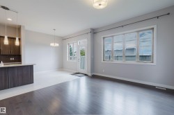 Spacious open-concept living area featuring dark wood-finish flooring, a large multi-pane window, and a glass-paned exterior door - 