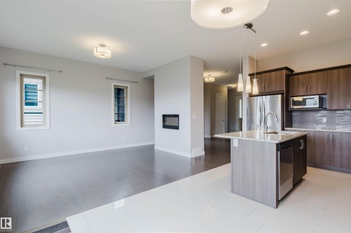 Open concept living area featuring a kitchen island with sink and pendant lighting, stainless steel appliances, wood-finish cabinetry, and a modern fireplace - 2921 Anderson Crest, Edmonton, AB 