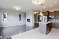 Open concept living area featuring a kitchen island with sink and pendant lighting, stainless steel appliances, wood-finish cabinetry, and a modern fireplace - 