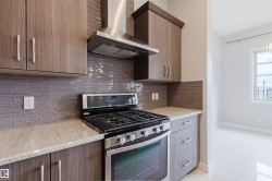 Kitchen showcasing a stainless steel range with a coordinating hood, light-toned countertops, and a gray horizontal tile backsplash - 