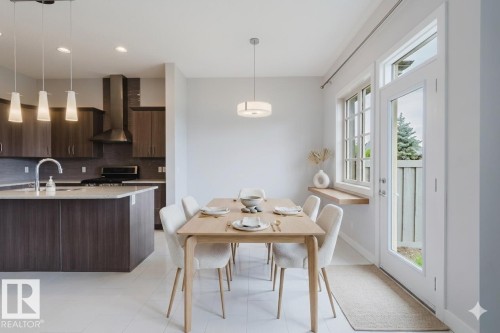 Bright dining area featuring a light wood-finish table, white tile flooring, and a contemporary pendant light fixture - 2921 Anderson Crest, Edmonton, AB 