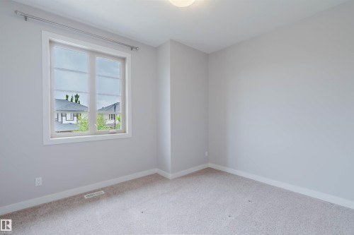Bright interior room featuring a large window with white trim, neutral wall tones, light-colored carpeting, and a flush-mount ceiling light fixture - 2921 Anderson Crest, Edmonton, AB 