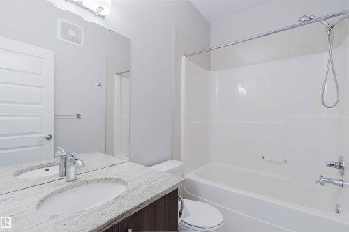 Full bathroom featuring a white tub/shower combination, chrome fixtures, a wood-finish vanity with a light-colored countertop, and a large wall-mounted mirror - 2921 Anderson Crest, Edmonton, AB 