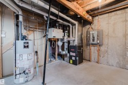 Utility room featuring a water heater, furnace, electrical panel, and exposed concrete walls - 