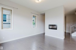 Living area featuring a sleek built-in fireplace, two windows with light-colored frames, wood-finish flooring, and white baseboards - 