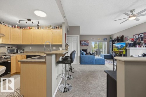 Open-concept kitchen featuring light wood cabinetry, a peninsula with seating, and stainless steel appliances - 71 3040 Spence Wynd, Edmonton, AB 
