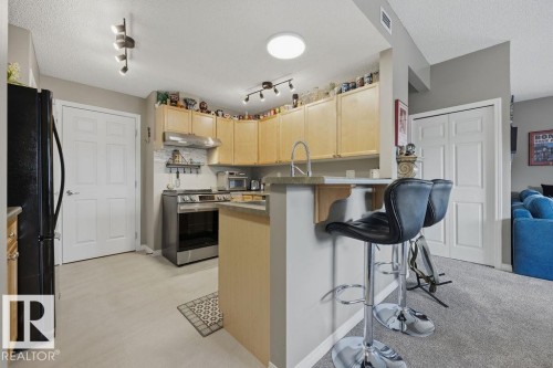Kitchen featuring light wood cabinetry, stainless steel range, and a breakfast bar with countertop seating - 71 3040 Spence Wynd, Edmonton, AB 