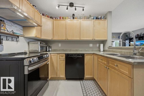 Kitchen featuring light wood cabinetry, stone-finish countertops, stainless steel range with hood, black dishwasher, and a double basin sink with a gooseneck faucet - 71 3040 Spence Wynd, Edmonton, AB 