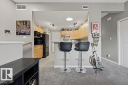 Open concept kitchen with a breakfast bar, light wood cabinetry, black appliances, and grey flooring - 
