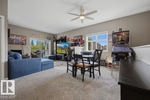 Carpeted living area featuring a ceiling fan, a sliding glass door leading to an outdoor deck, and a white-framed window - 71 3040 Spence Wynd, Edmonton, AB 