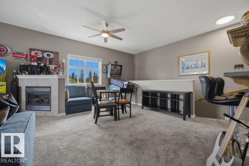 Carpeted open-concept room featuring a fireplace with a stone surround and mantel, a ceiling fan, a window, and a half-wall with a built-in shelving unit - 71 3040 Spence Wynd, Edmonton, AB 