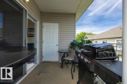 Covered outdoor patio area featuring neutral-toned siding, a sliding glass door, and an exterior door - 