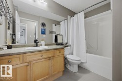 Bathroom featuring a light wood-finish vanity with a single basin sink, a large wall-mounted mirror, a toilet, and a combined bathtub and shower unit - 