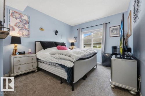 Carpeted bedroom featuring a window with exterior views, light blue wall paint, and a textured ceiling - 71 3040 Spence Wynd, Edmonton, AB 