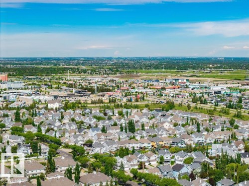 Expansive aerial perspective showcasing a residential development with various architectural styles, extensive green spaces, and a commercial sector in the background - 71 3040 Spence Wynd, Edmonton, AB 