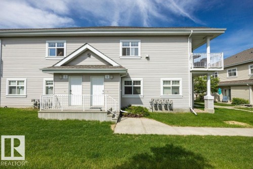 Two-story residential building featuring light-toned siding, white trim windows, and a prominent front porch with white railings - 71 3040 Spence Wynd, Edmonton, AB 