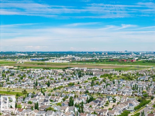 Expansive aerial perspective showcasing a residential development with a variety of single-family homes, green spaces, and a distant urban skyline - 71 3040 Spence Wynd, Edmonton, AB 