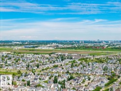 Expansive aerial perspective showcasing a residential development with a variety of single-family homes, green spaces, and a distant urban skyline - 