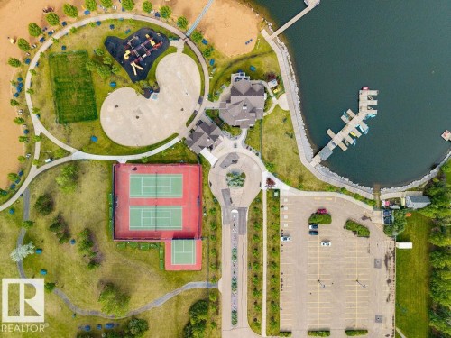 Aerial overview showcasing extensive recreational amenities including a waterfront with boat docks, multiple tennis courts, a playground area, and a large paved parking lot - 71 3040 Spence Wynd, Edmonton, AB 