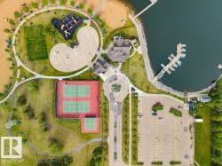 Aerial overview showcasing extensive recreational amenities including a waterfront with boat docks, multiple tennis courts, a playground area, and a large paved parking lot - 