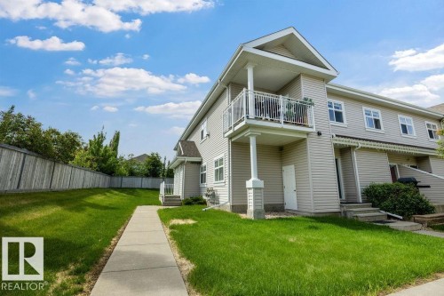 Exterior siding residence featuring a second-story balcony with white railing, a private concrete walkway, a fenced yard, and multiple windows - 71 3040 Spence Wynd, Edmonton, AB 