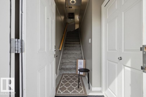 Interior entryway with neutral gray walls, a carpeted staircase, and a light wood-finish handrail - 71 3040 Spence Wynd, Edmonton, AB 