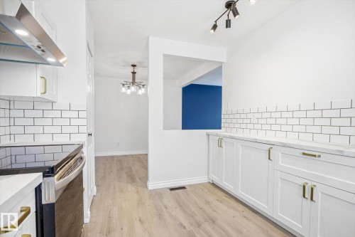 Bright kitchen featuring white shaker cabinetry, gold-tone hardware, subway tile backsplash, light wood-finish flooring, and a stainless steel range with overhead ventilation - 857 Erin Place, Edmonton, AB 