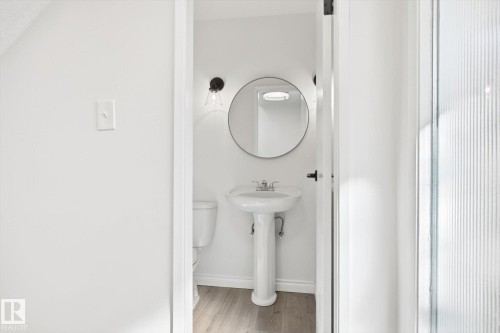 Pedestal sink with chrome faucet, circular mirror, and wall-mounted sconce lighting - 857 Erin Place, Edmonton, AB 