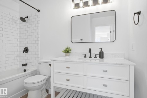 Bathroom featuring a white subway tile shower surround, matte black shower fixtures, a white vanity with a light-colored countertop, and a rectangular mirror with a black frame - 857 Erin Place, Edmonton, AB 
