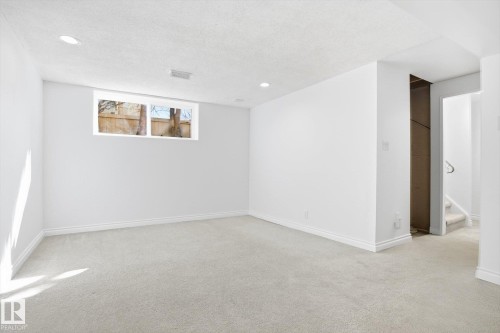 Spacious lower-level room featuring light neutral carpeting, white painted walls, recessed lighting, and a window providing natural light - 857 Erin Place, Edmonton, AB 