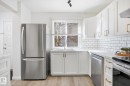 Kitchen featuring light wood-finish flooring, white cabinetry with gold-tone hardware, white subway tile backsplash, white countertops, and stainless steel appliances - 857 Erin Place, Edmonton, AB 