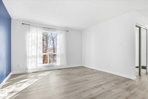Spacious room featuring light wood-finish flooring, a large window with white trim, and a mirrored sliding door - 857 Erin Place, Edmonton, AB 