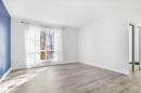 Spacious room featuring light wood-finish flooring, a large window with white trim, and a mirrored sliding door - 857 Erin Place, Edmonton, AB 